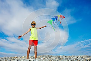 Smiling boy stand on pebble beach holding many colorful kites