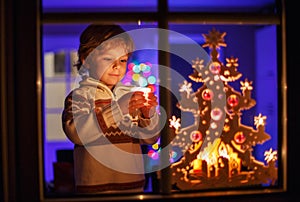 Smiling boy standing by window at Christmas time and holding can