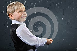 Smiling boy stands in rain and catches drops