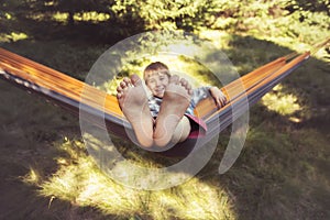 Smiling boy is swinging in a hammock. His feet are close up