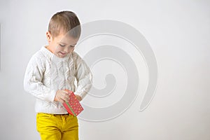 A smiling boy is takes out a gift. Child looking of a red cardb