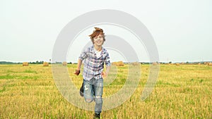 Smiling boy teenager running on harvesting field on haystack background in village. Cheerful teenager boy running on