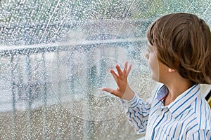 Smiling boy watching the rain outside at a window
