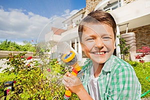 Smiling boy watering garden using hand sprinkler