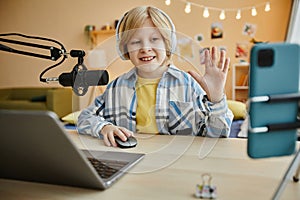 Smiling boy waving hand to online audience while making livestream