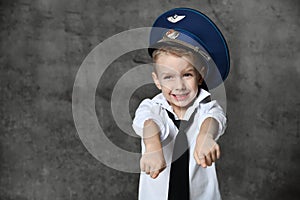 Smiling boy in white shirt, jeans, tie and police cap standing and playing in policeman over grey background