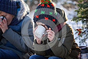 Smiling boy on a winter walk outdoors drinking chocolate in sunny day