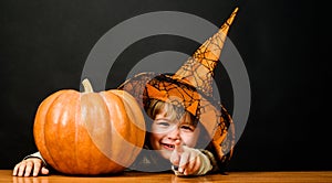 Smiling boy in witch hat with halloween pumpkin pointing to you. Trick or treat. Little kid with pumpkin. Preparation