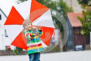 Smiling boy with yellow umbrella and colorful jacket outdoors at