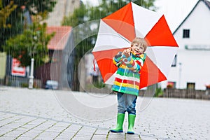 Smiling boy with yellow umbrella and colorful jacket outdoors at