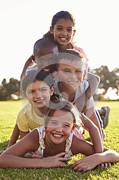 Smiling boys and girls lying in a pile on grass in Summer