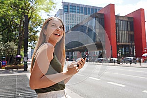 Smiling Brazilian woman hail a vehicle using mobile app waiting for taxi or uber on Paulista Avenue, Sao Paulo, Brazil photo