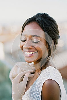 Smiling bride in gloves touches her collarbones with her hands. Portrait