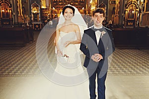 Smiling bride and groom walk out of the church