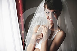 Smiling bride is posing in whiteness on the background curtains