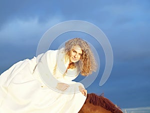 Smiling bride ride on horse at dramatic sky backgr