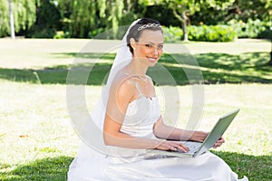 Smiling bride using laptop in garden