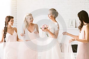 Smiling bridesmaids holding the dress of the bride