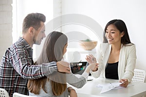 Smiling broker giving keys from first house to millennial couple