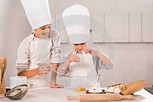 smiling brother and sister in aprons and chef hats during food preparation at table