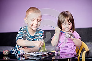 Smiling brother and sister with water colors, coloring Easter eggs