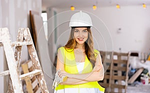 Smiling brown-haired female architect in yellow vest and helmet at construction site