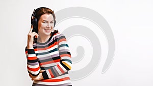 smiling brown-haired woman in multi-colored dress listens to music in closed isodynamic headphones. Medium shot portrait