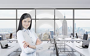 Smiling brunette business lady with cross hands is standing in a modern panoramic office in New York City. Manhattan panoramic vie