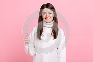 Smiling brunette female showing thumb up to camera, expressing approbation and positive emotions.