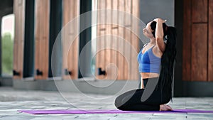 Smiling brunette fitness woman stretching neck before training sitting on floor mat outdoor building