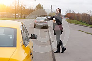 Smiling brunette with long hair stop yellow taxi in autumn