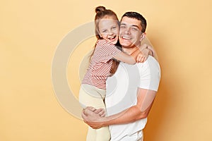 Smiling brunette man holding his little daughter, child hugging her father family looking at camera with happy faces standing in