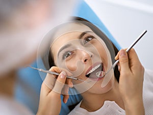 Smiling brunette woman being examined by dentist at dental clinic. Hands of a doctor holding dental instruments near