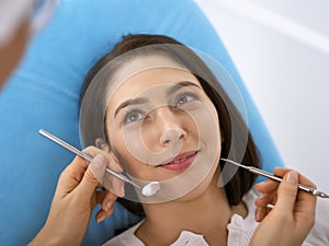 Smiling brunette woman being examined by dentist at dental clinic. Hands of a doctor holding dental instruments near