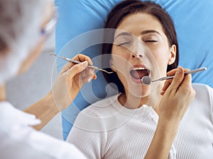 Smiling brunette woman being examined by dentist at dental clinic. Hands of a doctor holding dental instruments near