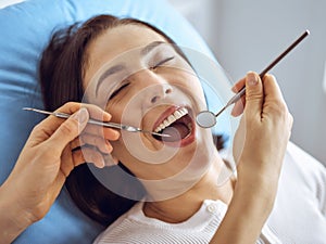 Smiling brunette woman being examined by dentist at dental clinic. Hands of a doctor holding dental instruments near