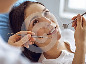 Smiling brunette woman being examined by dentist at dental clinic. Hands of a doctor holding dental instruments near