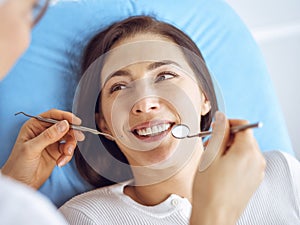 Smiling brunette woman being examined by dentist at dental clinic. Hands of a doctor holding dental instruments near