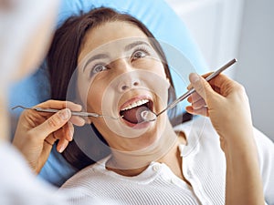 Smiling brunette woman being examined by dentist at dental clinic. Hands of a doctor holding dental instruments near