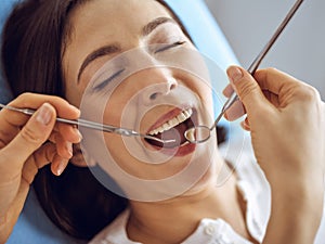 Smiling brunette woman being examined by dentist at dental clinic. Hands of a doctor holding dental instruments near