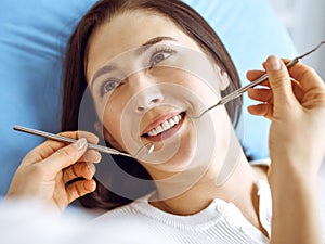 Smiling brunette woman being examined by dentist at dental clinic. Hands of a doctor holding dental instruments near