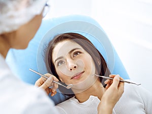 Smiling brunette woman being examined by dentist at dental clinic. Hands of a doctor holding dental instruments near