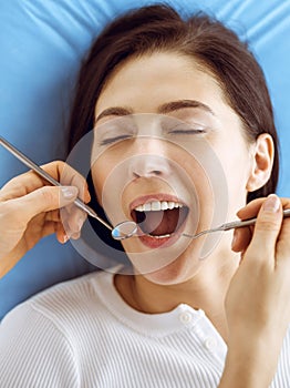 Smiling brunette woman being examined by dentist at dental clinic. Hands of a doctor holding dental instruments near