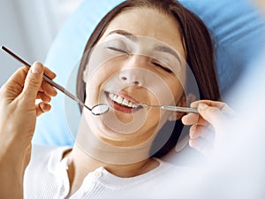 Smiling brunette woman being examined by dentist at dental clinic. Hands of a doctor holding dental instruments near