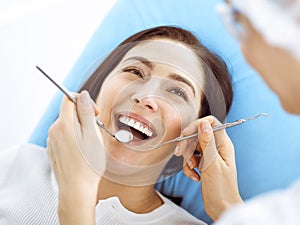 Smiling brunette woman being examined by dentist at dental clinic. Hands of a doctor holding dental instruments near