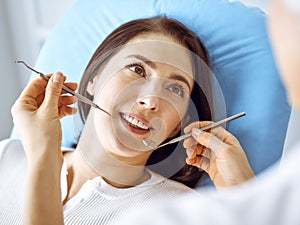 Smiling brunette woman being examined by dentist at dental clinic. Hands of a doctor holding dental instruments near