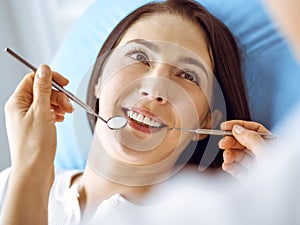 Smiling brunette woman being examined by dentist at dental clinic. Hands of a doctor holding dental instruments near