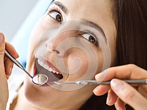 Smiling brunette woman being examined by dentist at dental clinic. Hands of a doctor holding dental instruments near