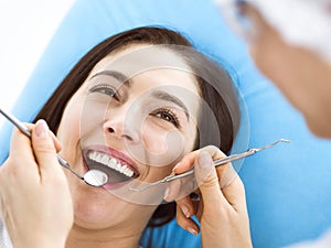 Smiling brunette woman being examined by dentist at dental clinic. Hands of a doctor holding dental instruments near