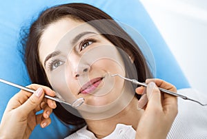 Smiling brunette woman being examined by dentist at dental clinic. Hands of a doctor holding dental instruments near